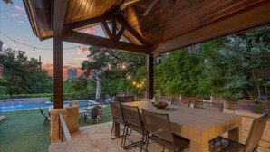 Eine Terrasse im Freien mit Holztisch und -stühlen, umgeben von Steinböden und viel Grün.