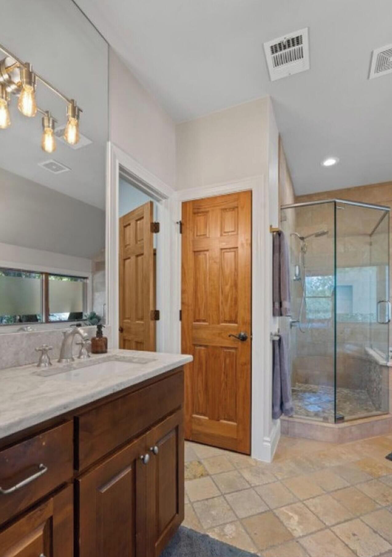 Une salle de bain moderne avec un grand meuble-lavabo, une cabine de douche en verre et une porte en bois.