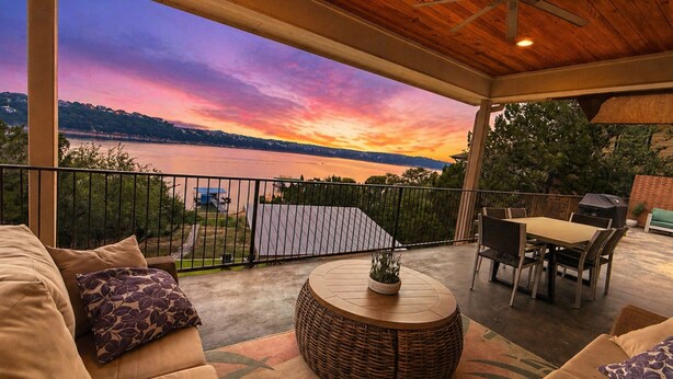A covered outdoor seating area with a view of a sunset over a body of water, a dining table, and a grill. - Lake House Dock Slip Heated Pool Boat Launch Beach Game Room (Leander)