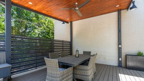 En udendørs patio med træterrasse, et bord med stole, en loftventilator og en lygte.