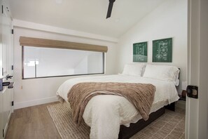 Ein Schlafzimmer mit einem großen Fenster, einem Bett mit brauner Decke und zwei grünen Wandbildern.
