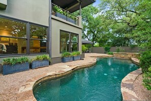Une maison moderne dotée d’une piscine, de grandes fenêtres et d’un balcon agrémenté de plantes.