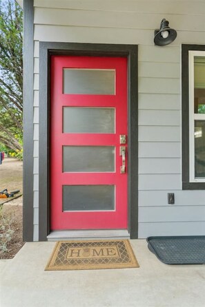 A red door with a glass panel, a doormat with 'HOME' written on it, and a black mailbox.