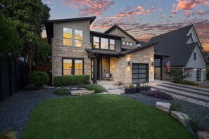 A modern two-story house with a stone facade, a front porch, and a well-maintained lawn. - Zilker Home With Heated Pool Hot Tub Walkable (Austin)
