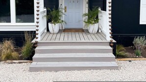 Uma casa com varanda frontal, uma porta branca e dois vasos de plantas em cada lado.