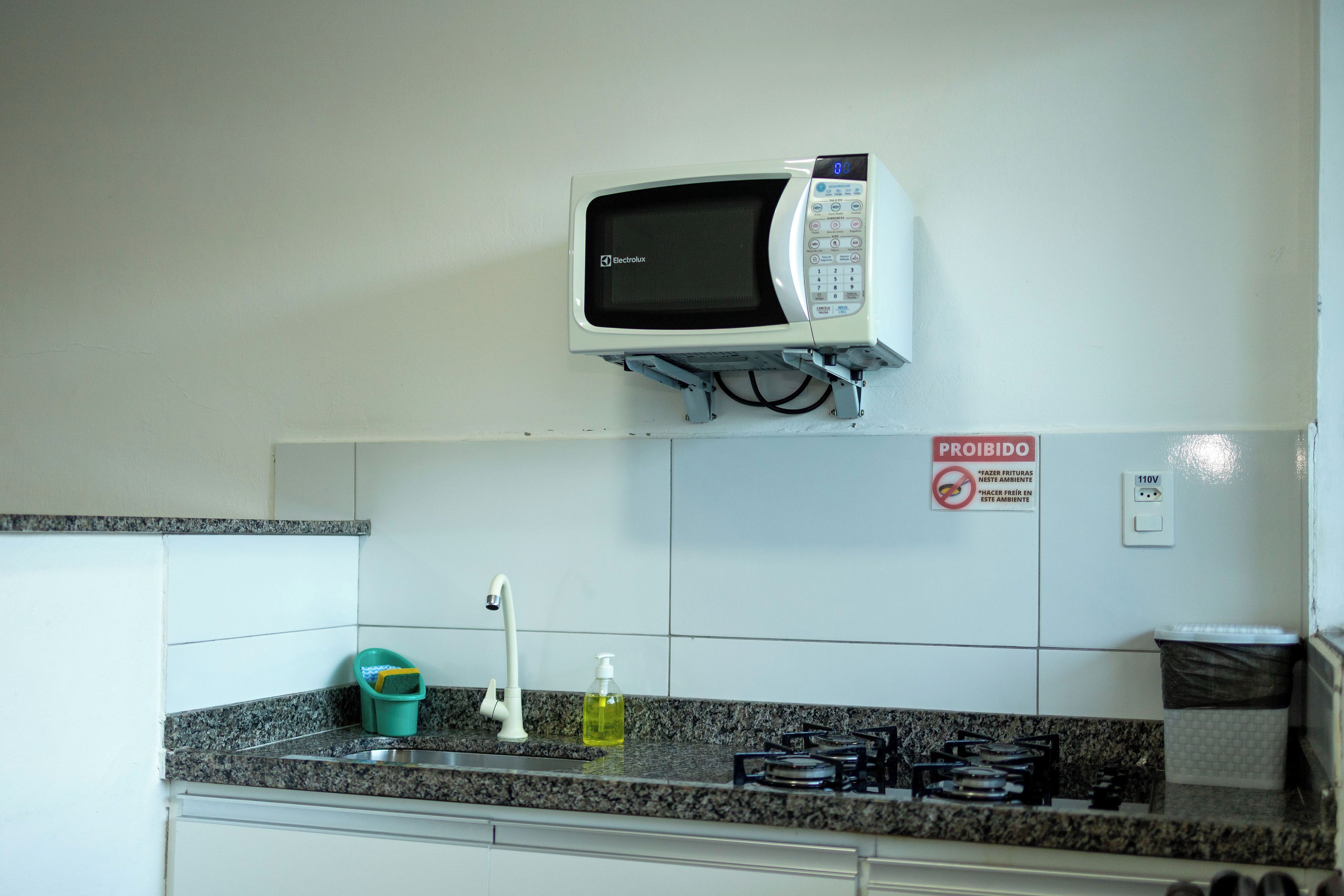 Una cocina equipada con microondas, lavamanos, grifo y un letrero que indica 'No Fumar'.