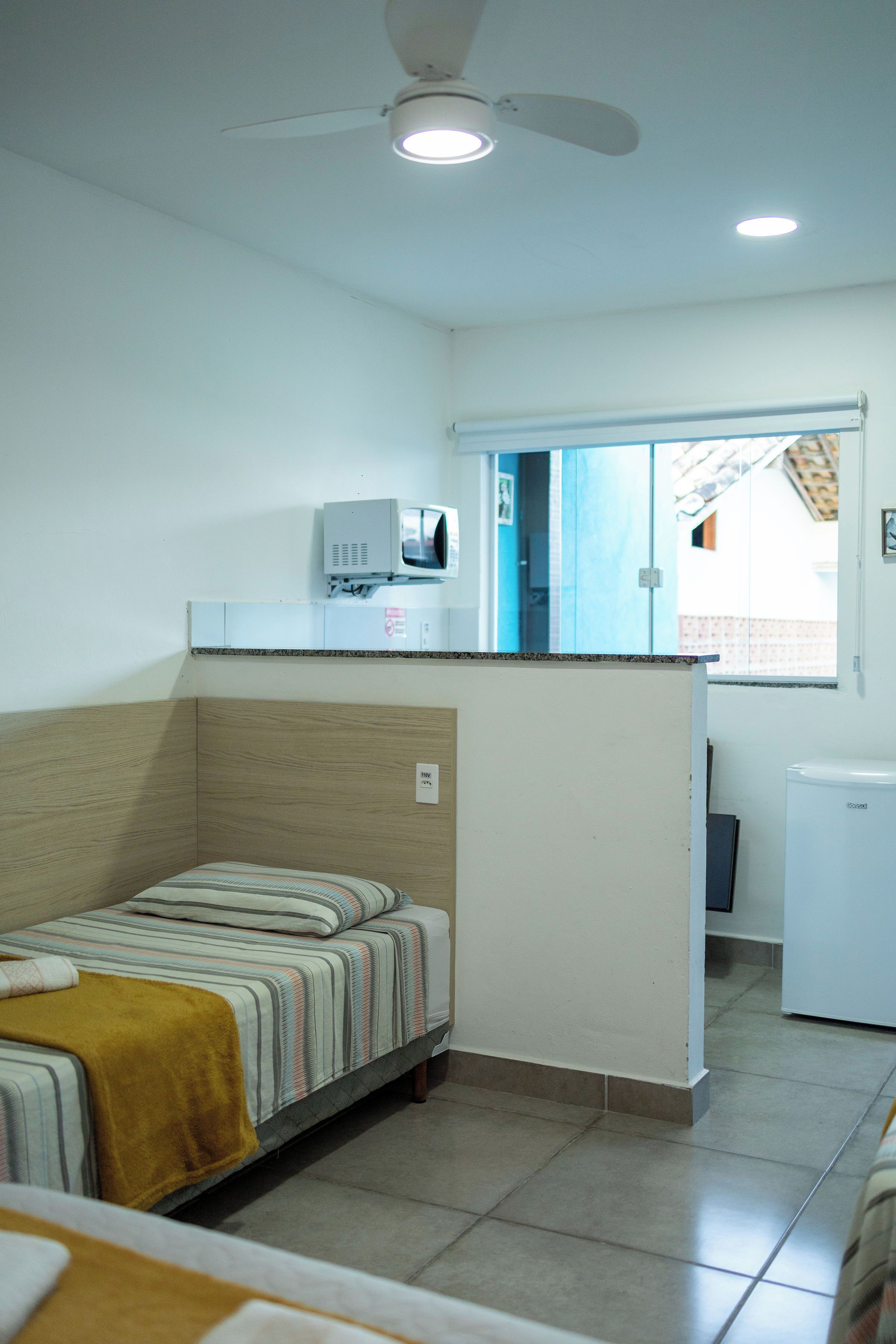 Habitació compacte amb llit, una cuineta petita, ventilador de sostre i finestra amb vistes a l'exterior.