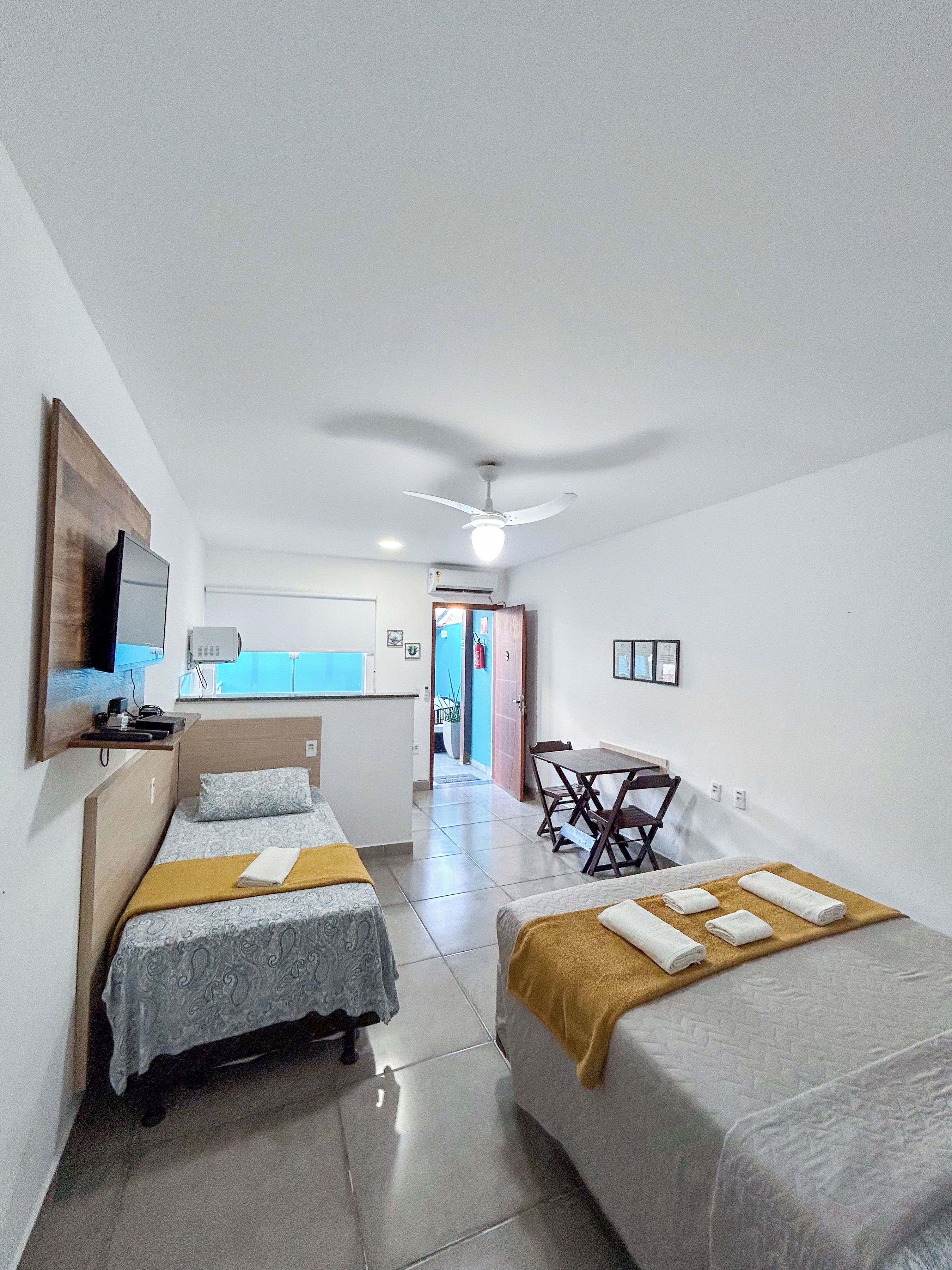 A hotel room with two beds, a desk, a chair, a TV, and a ceiling fan.