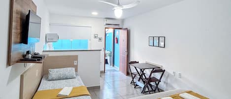 A hotel room with two beds, a desk, a chair, a TV, and a ceiling fan.