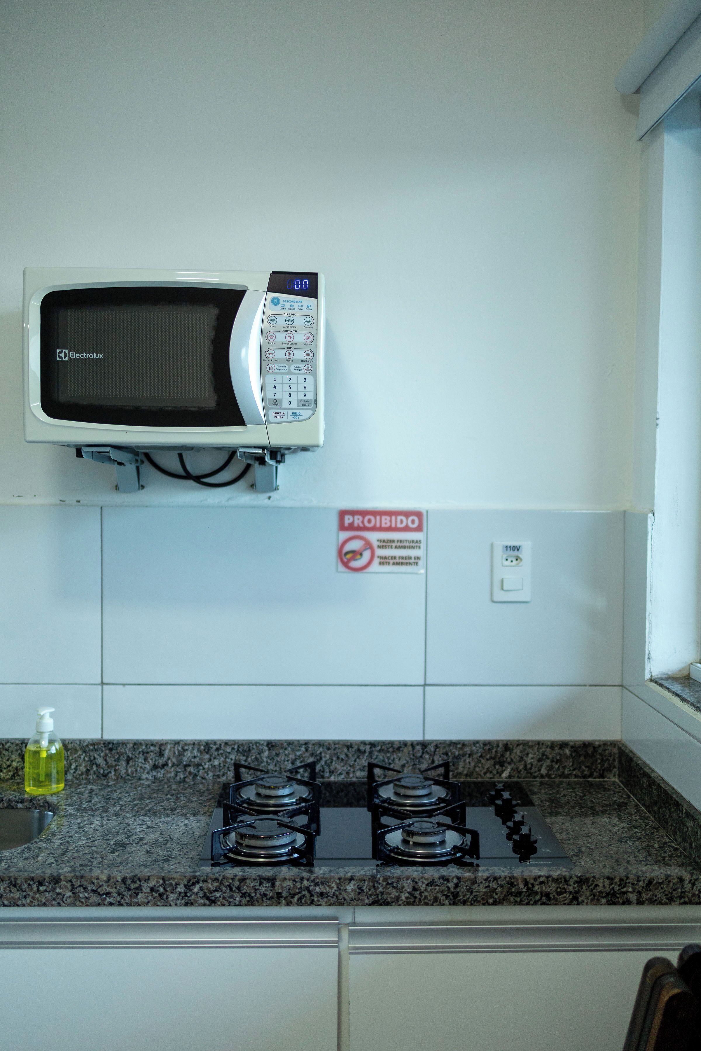 A kitchen with a microwave, stove, and a 'PROHIBIDO' sign.