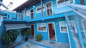 Um edifício de dois andares com fachada azul, uma varanda e plantas em vasos.
