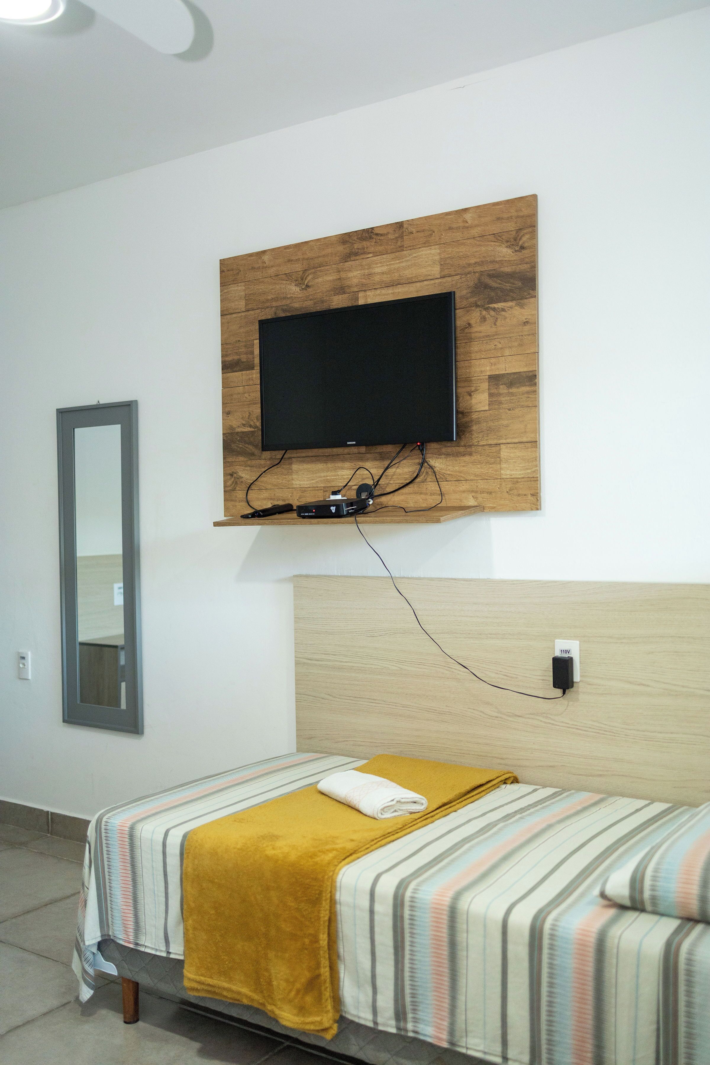 Une chambre à coucher avec un lit, un téléviseur fixé au mur et un miroir.