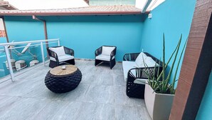 A rooftop patio with outdoor furniture, a potted plant, and a tiled floor.
