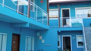 Um edifício de dois andares com fachada azul, porta de madeira e varanda com guarda-corpo de vidro.