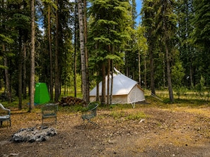 Una tienda de campaña montada en un bosque, con una pila de leña y una silla verde cerca.