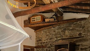 A rustic room with a stone wall, a bed with a green headboard, a wooden ceiling, and a white canopy over the bed. - La Cannicciaia "Historic House Near Florence" (Tobbiana)