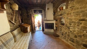 A rustic stone interior with a fireplace, a sofa, and a door leading outside. - La Cannicciaia "Historic House Near Florence" (Tobbiana)