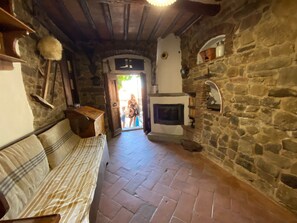 Ein rustikaler Innenraum aus Stein mit Kamin, einer Couch und einer Tür, die nach draußen führt.