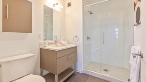 Een moderne badkamer met een douche met glazen wand, een wastafel met spiegel en een toilet.