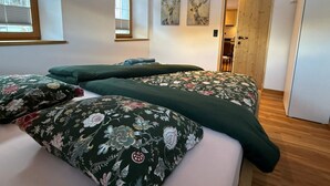 Quarto com duas camas, uma janela e porta que dá para outro espaço.