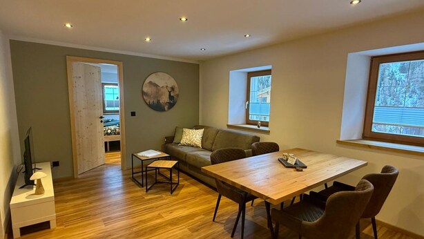 Uma sala de estar moderna com uma mesa de jantar de madeira, um sofá e uma televisão.