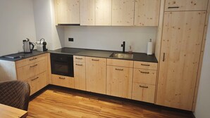 Uma cozinha compacta com armários de madeira, bancada preta, pia, lava-louças e cafeteira.