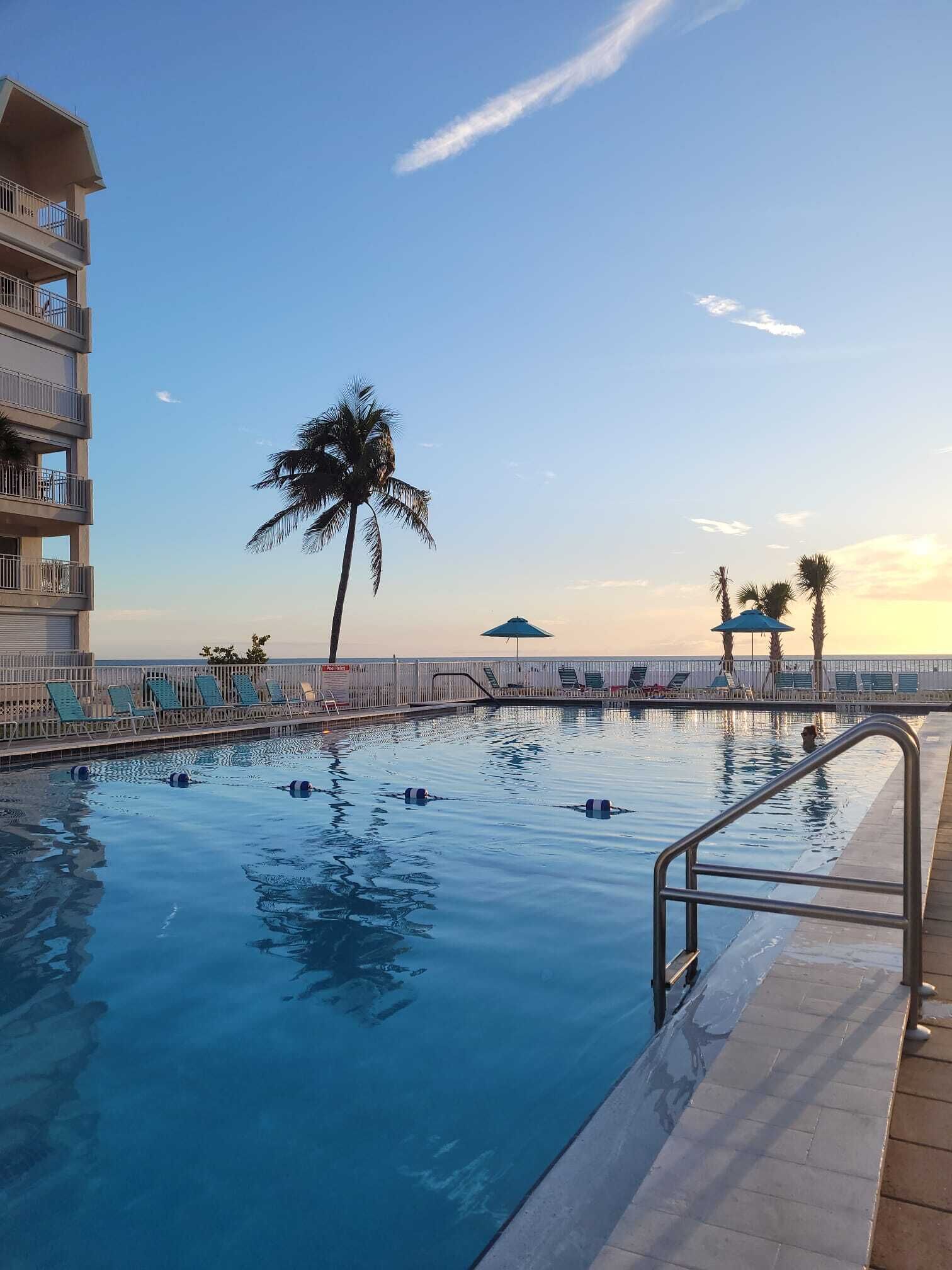 A swimming pool with lounge chairs, palm trees, and a building with balconies.