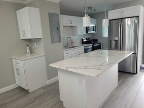 A modern kitchen with white cabinetry, a marble island, stainless steel appliances, and pendant lighting. - Beachfront Condo Leonardo (Fort Myers Beach)