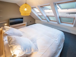 A bedroom with a bed, a TV, a hanging light fixture, and skylights.