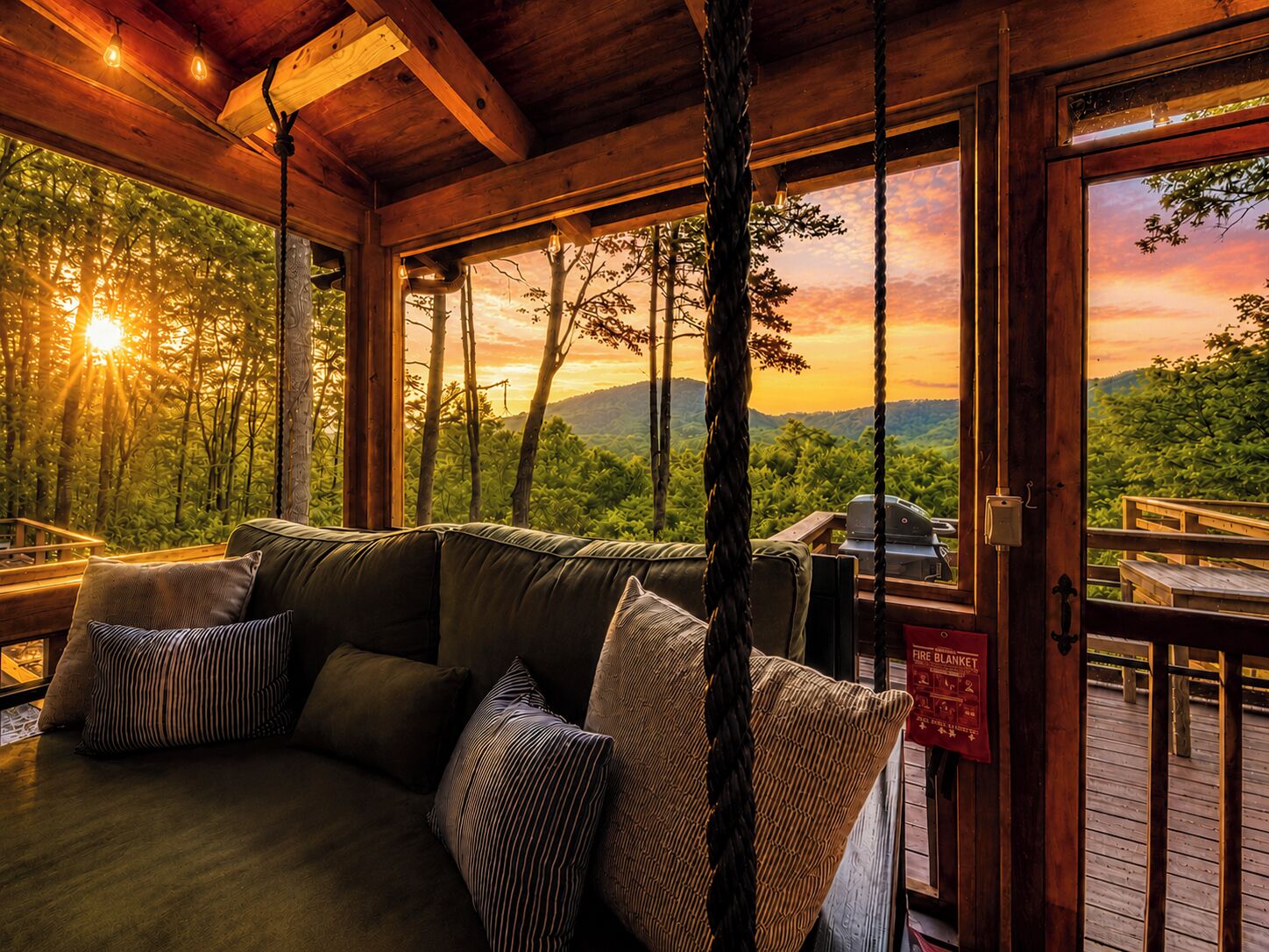 A wooden cabin with a sofa, pillows, and a view of a forest and mountains.