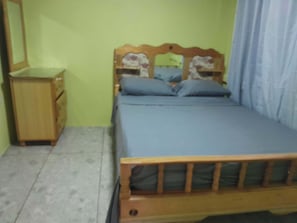 Quarto com estrutura de cama de madeira, mesa de cabeceira e cômoda.