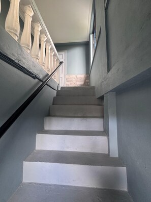 Uma escadaria com degraus brancos que leva a um patamar, com paredes adornadas por um detalhe em pedra e um corrimão com colunas.