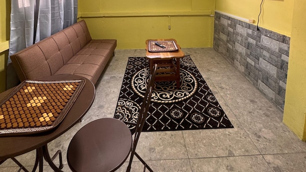 A living room with a sofa, a small table with a mat, a TV mounted on the wall, and a window with curtains.