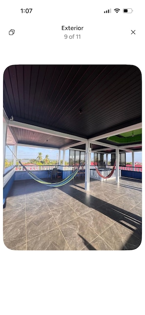 Uma área externa coberta com uma rede, piso de azulejos e vista da paisagem ao redor.