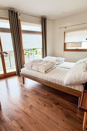 A bedroom with a wooden bed, large windows, and a view of the outdoors.