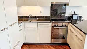A compact kitchen with white cabinets, a stainless steel stove, and a wooden herringboard floor. - Haus zum Alpenblick - Wannenhorn by Interhome (Bellwald)