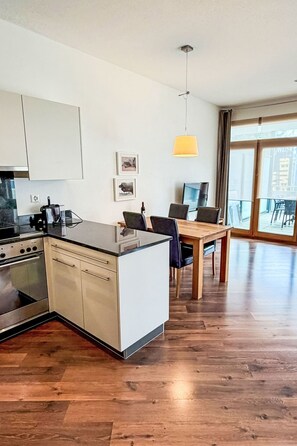 A modern kitchen with a central island, a dining area with a wooden table, and large windows offering a view.
