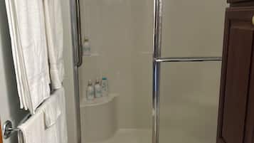 Ducha con puerta de vidrio, inodoro blanco y toallero con toallas.