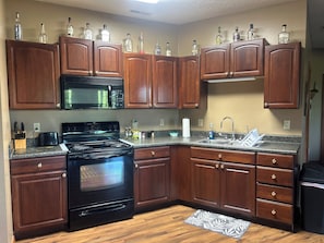 A kitchen with wooden cabinets, a black stove, a microwave, and a sink. - Rent the entire private basement level. Enjoy a peaceful country setting. (Owenton)