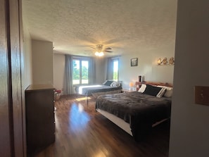 Une chambre avec un lit, un bureau et une chaise. Il y a une fenêtre avec des rideaux, un ventilateur de plafond et un tableau accroché au mur.