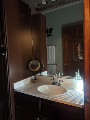 Ein Badezimmer mit einem Holzlagerfläschchen, einem Waschbecken mit Spiegel und einem Handtuchhalter.