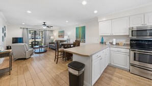 A modern kitchen with white cabinets, a stainless steel oven, and a dining area with a table and chairs. - Seaside Beach & Racquet 2101 (Orange Beach)