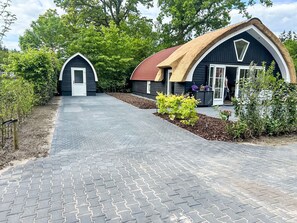 A pathway leading to a building with a thatched roof and a smaller structure with a white door.