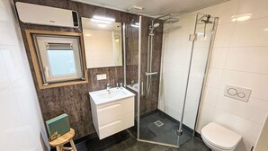 Un baño moderno con cabina de ducha de vidrio, un lavamanos blanco y un inodoro.