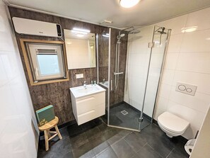 Uma casa de banho moderna com cabine de duche em vidro, lavatório branco e sanita.