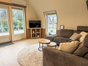 Un salon avec un canapé, un téléviseur, une petite table et une fenêtre donnant sur des arbres.