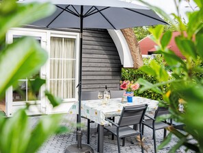 An outdoor patio with a table set for two, a bottle of white wine, and a vase with flowers.