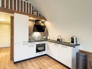 A modern kitchen with white cabinetry, a built-in oven, a stovetop, and a coffee machine.