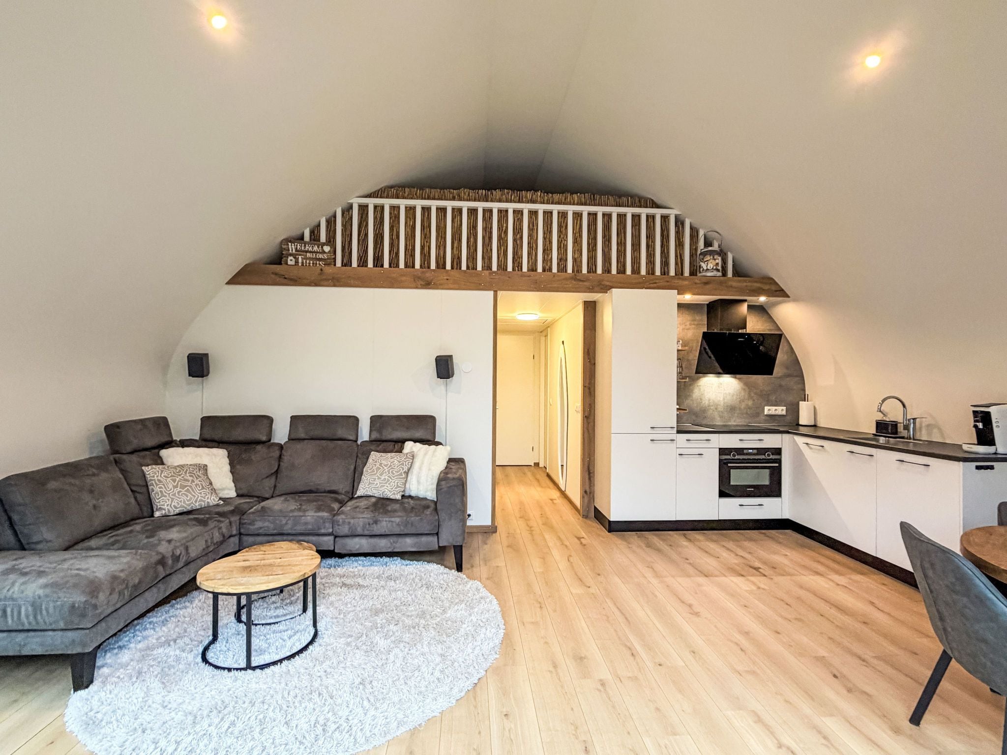 Un espacio habitable tipo loft con sofá, mesa de centro y zona de cocina con horno y microondas integrados.