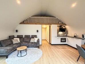 A loft-style living space with a sofa, coffee table, and a kitchen area with a built-in oven and microwave.
